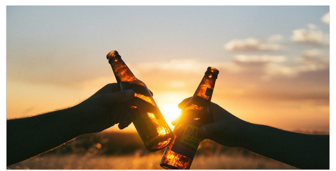 Two beer bottles clinking at sunset